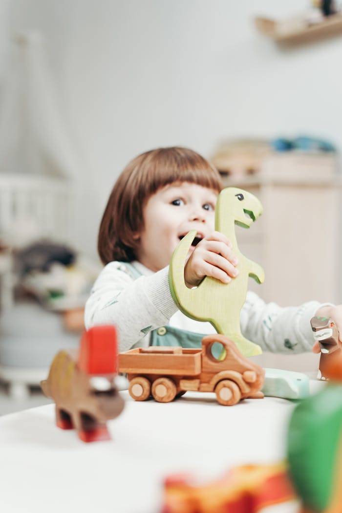 A cheerful child engages in imaginative play with wooden dinosaur toys indoors.